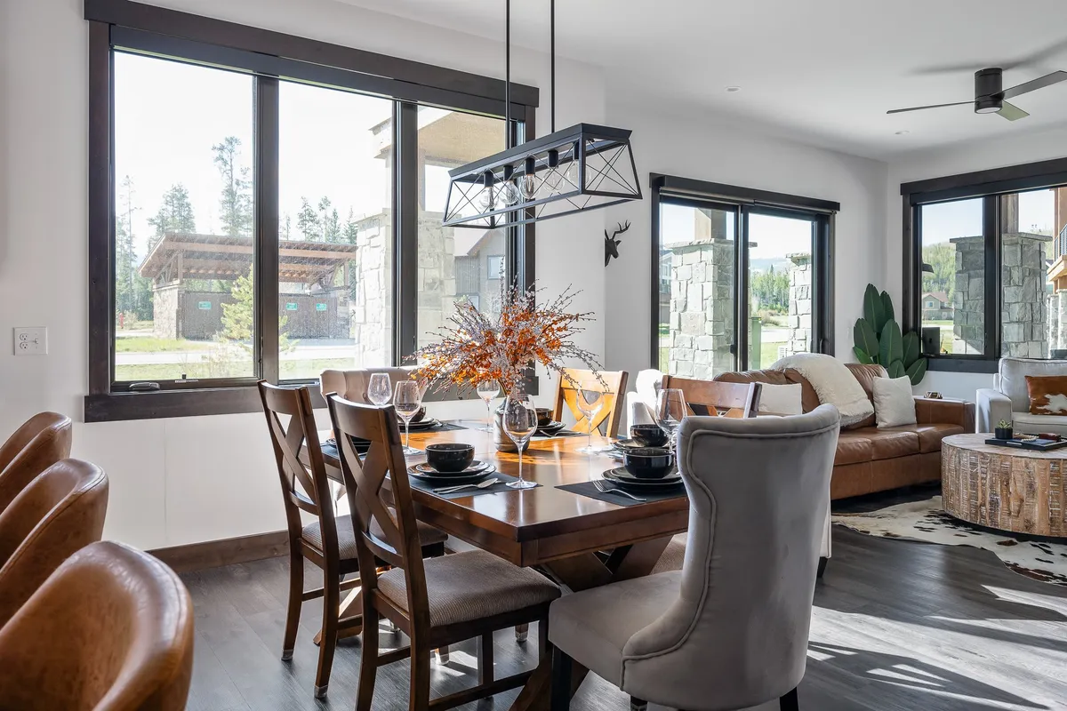 A beautifully set dining table in front of large windows, adjacent to comfortable seating and a decorative plant. The scene feels warm and welcoming, ideal for family meals or casual conversations, with natural light streaming in and a clear visual connection to the outdoors.
