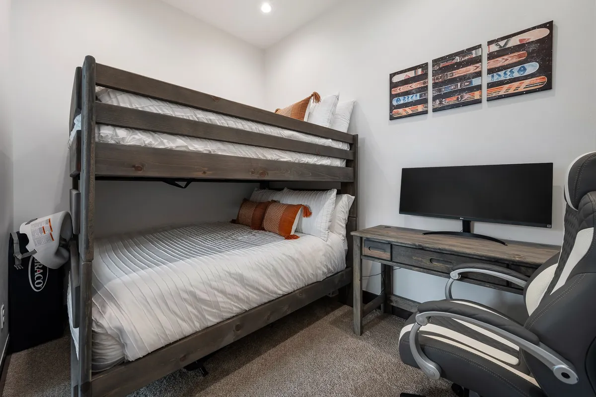 A practical bunk room setup with a sturdy full-over-full bunk bed, a functional desk complete with a monitor, and playful wall art. The design is both inviting and highly functional, catering to children, teens, or remote workers who need a comfortable and flexible space.