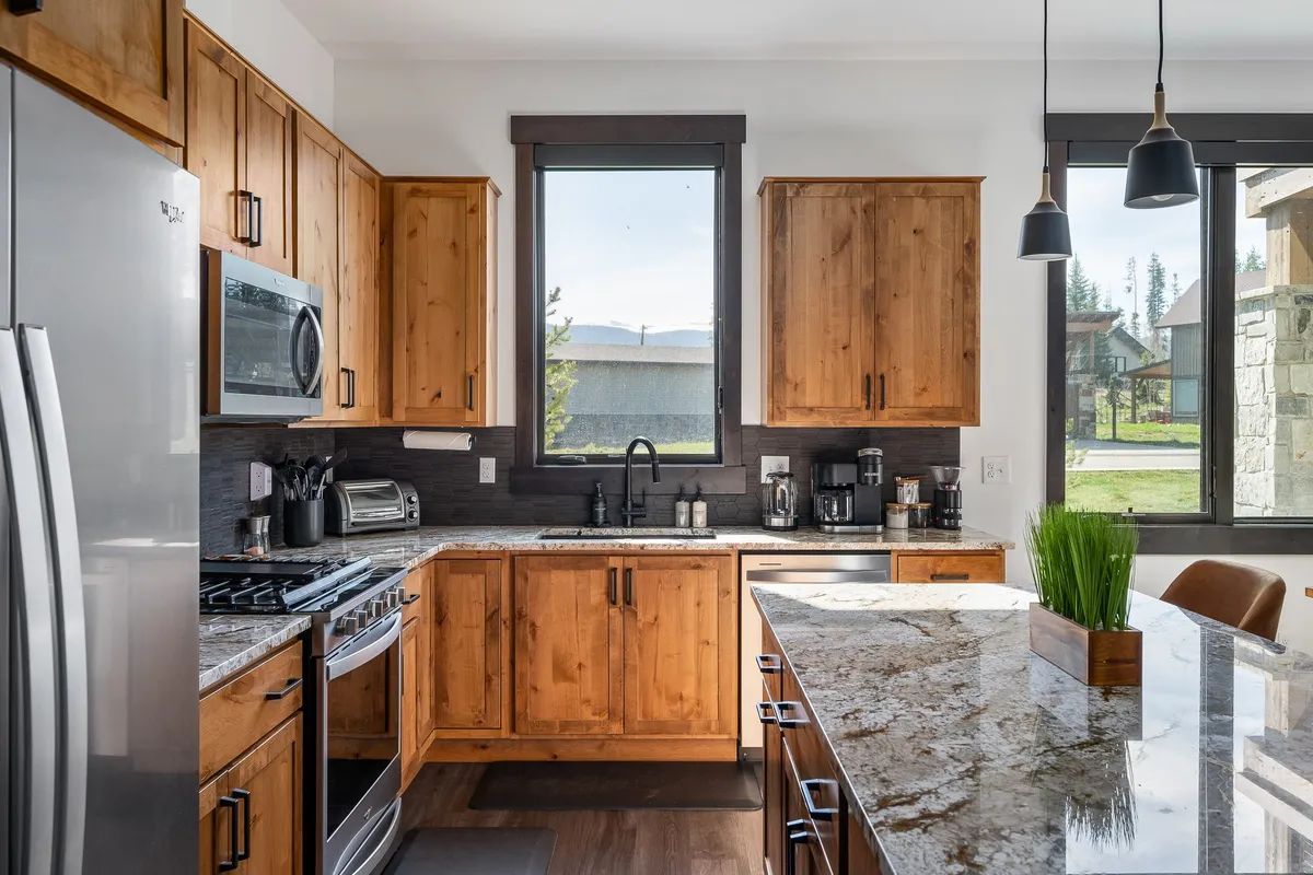 A warm, welcoming kitchen scene with granite countertops, wood cabinetry, a large window, and stainless steel appliances. The image exudes comfort and functionality, suitable for meal prep or socializing, and highlights the modern yet cozy ambiance.