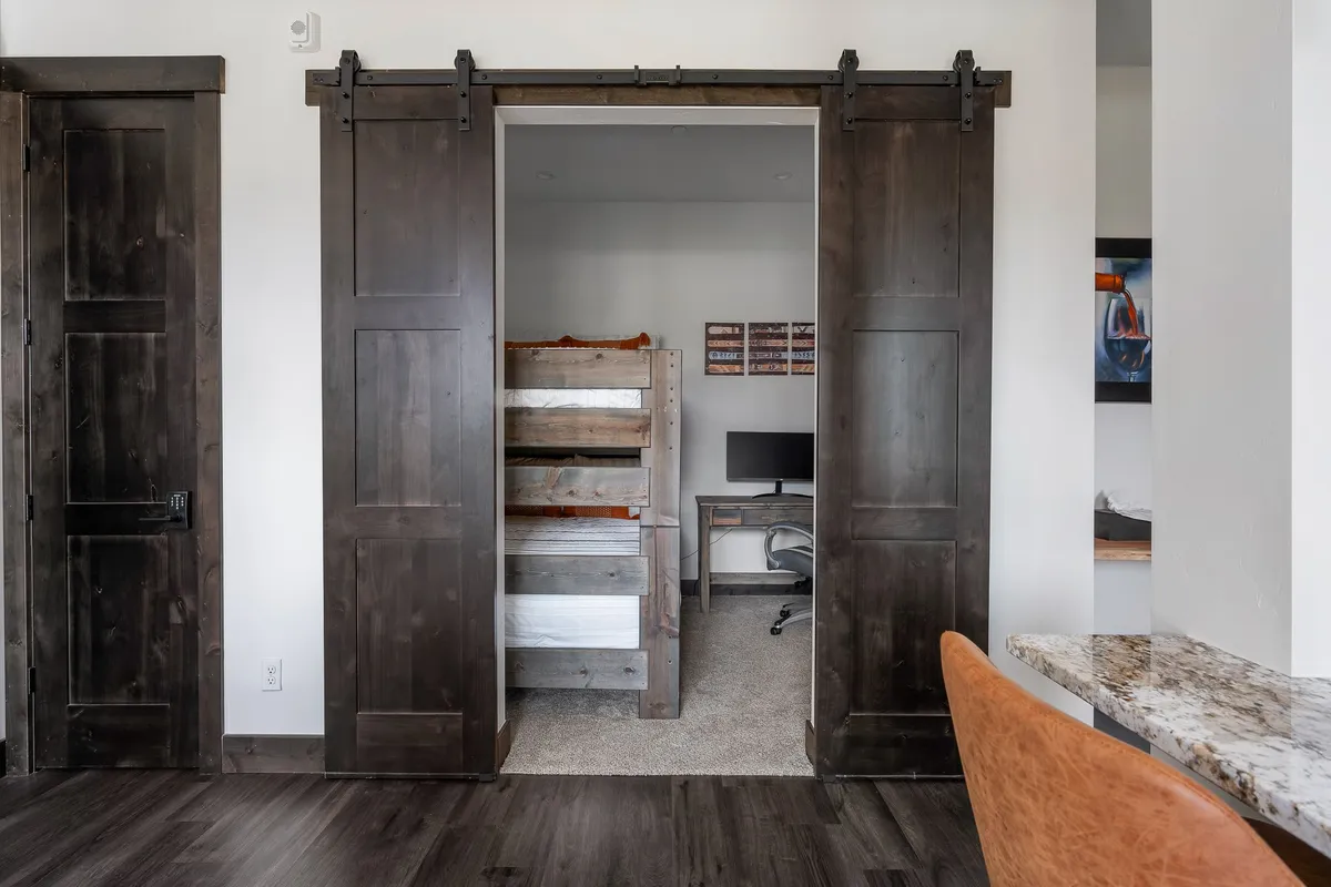 A versatile bonus bunk room featuring barn doors for privacy, two bunk beds suitable for children or extra guests, and a desk equipped with a computer. The space is styled for comfort and functionality, making it ideal for family game nights, study sessions, or remote work.