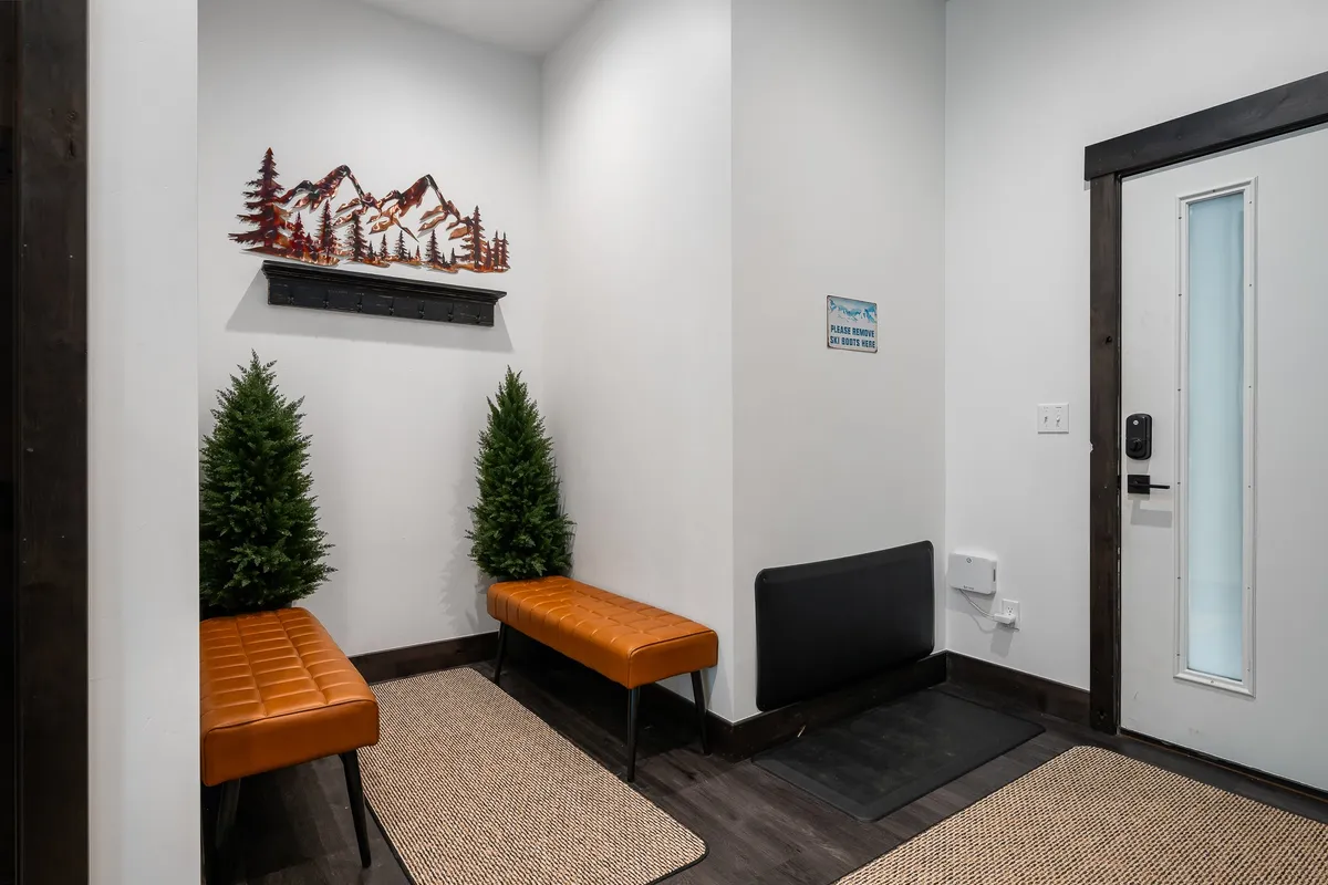 A welcoming entryway featuring mountain-themed wall art, orange benches for removing or putting on outdoor gear, and small decorative trees. The ambiance is cozy and inviting, evoking a sense of arrival and readiness for outdoor exploration.