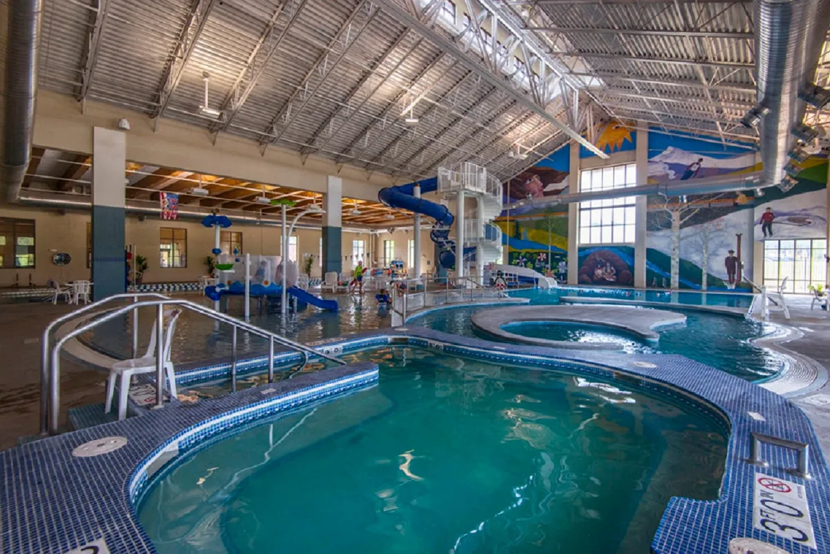 This vibrant interior image features a swimming pool, a colorful mural, a water slide, and children joyfully playing in the water. The lively environment exudes the fun and activity to be found at the Grand Park Rec Center, central to the family-friendly amenities discussed in the section.