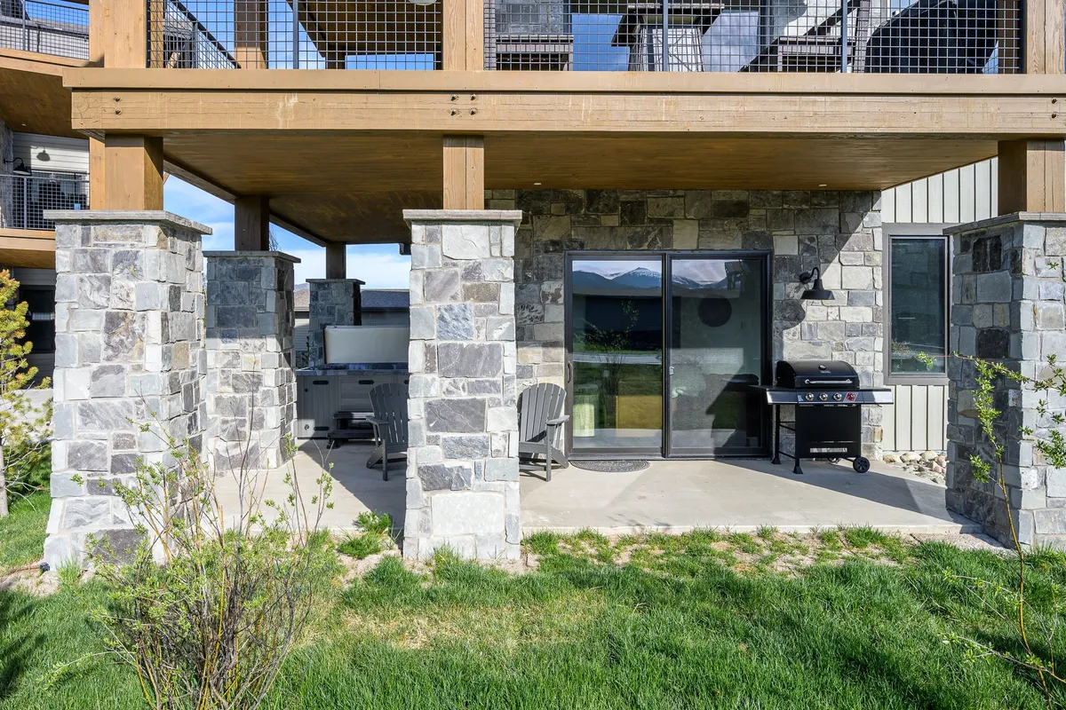 This exterior shot features a well-appointed patio with stone pillars, a grill, patio chairs, and a lush green lawn. The space is clearly designed for outdoor dining, barbecuing, and social gatherings, offering a seamless blend of relaxation and entertainment.