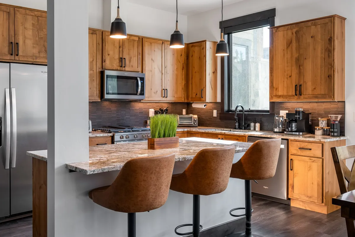 A wide view of a kitchen island equipped with bar stools, ample cabinetry, and a stylish countertop. The scene invites interaction, emphasizing the island as a central spot for socializing and shared culinary experiences.