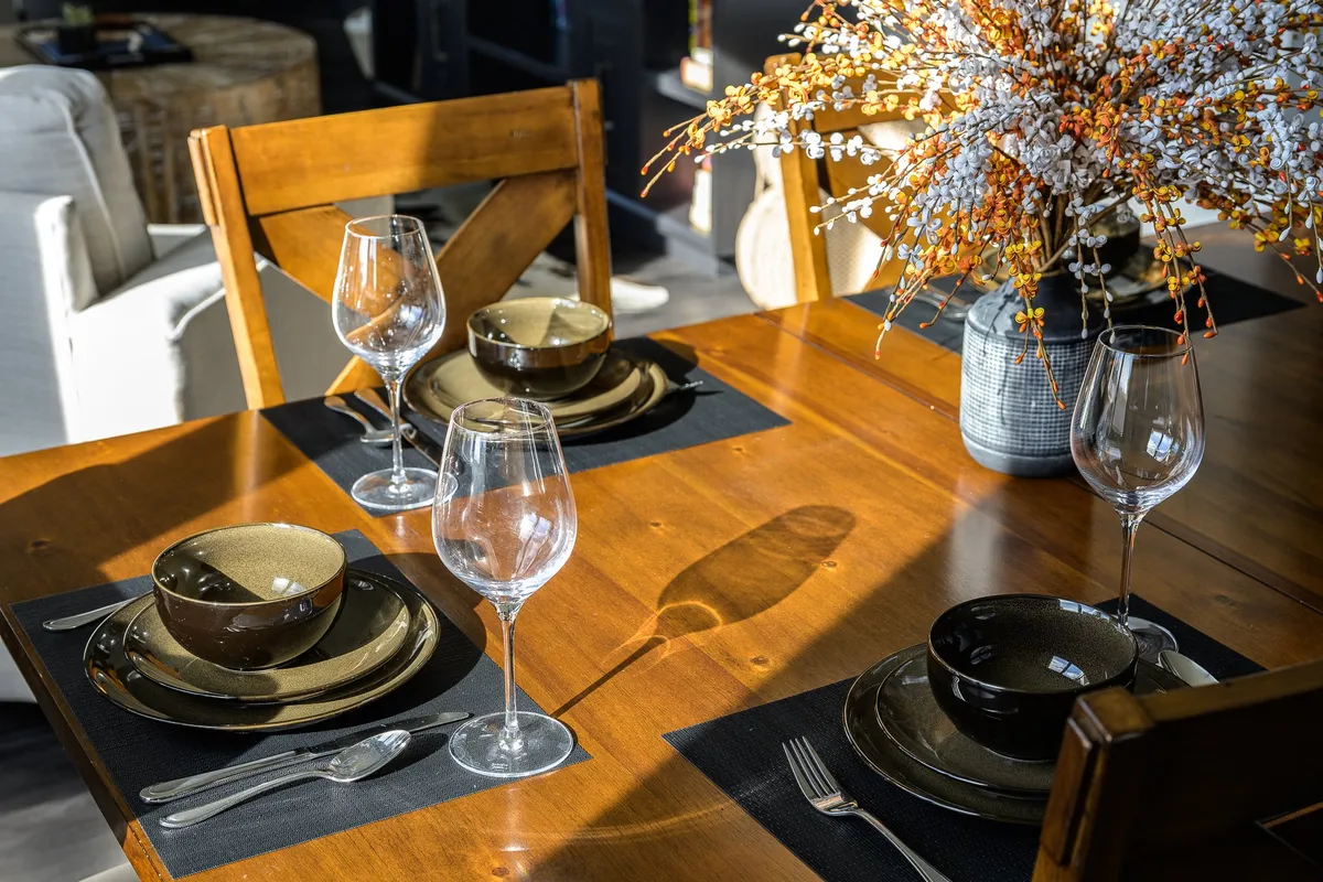 An elegantly set dining table with plates, glasses, a floral centerpiece, and wooden chairs, ready for a group meal. The scene radiates warmth and hospitality, inviting shared celebrations and memorable meals.