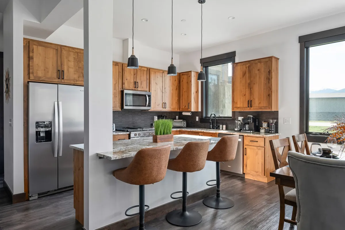A sun-filled gourmet kitchen featuring a sleek granite countertop, inviting bar stools at a spacious island, warm wooden cabinets, and large windows that let in natural light. The scene captures both the functional and social aspects of the kitchen, with space for cooking and gathering.