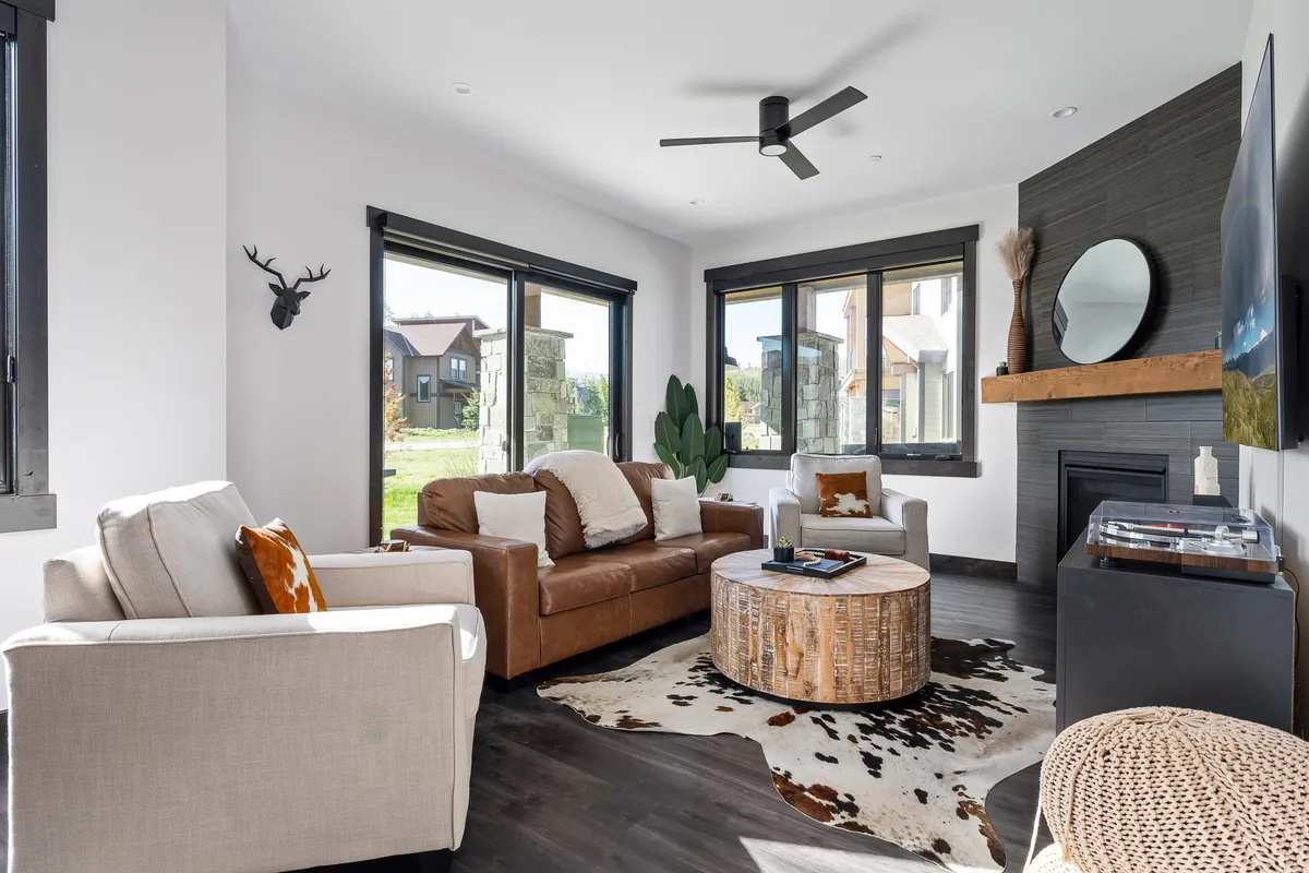 A bright and comfortable living room with a leather sofa, round coffee table, cowhide rug, fireplace, and large windows, creating a welcoming environment for relaxation and socializing after a day of adventures.